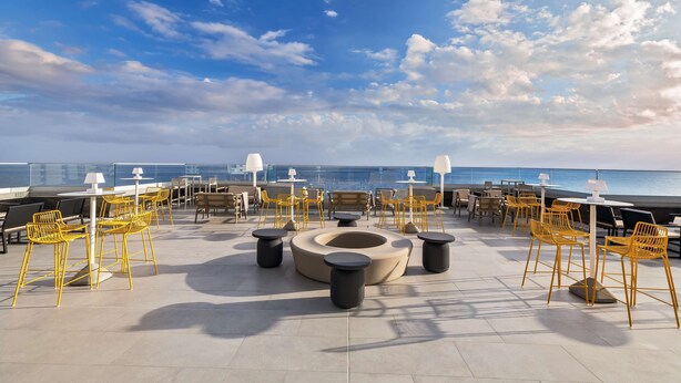 Una terraza en la azotea con sillas y mesas amarillas, un área de estar circular y vista al océano.