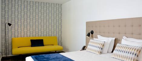 Een hotelkamer met een bed, een gele bank en een behang met een patroon.