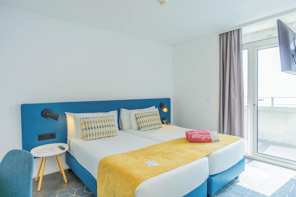 A hotel room with two beds, a small table, a chair, and a TV.
