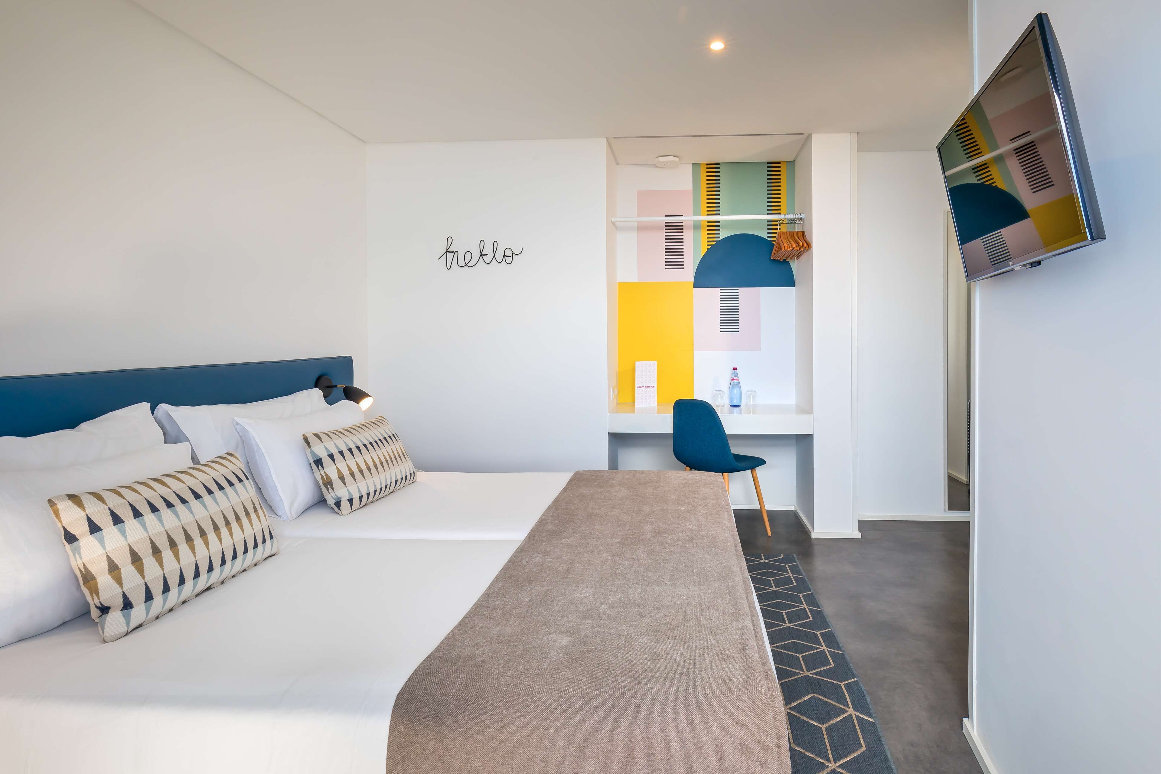 Una habitación de hotel moderna con una cama, un escritorio, una silla y un televisor fijado a la pared.