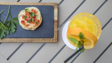 Un sándwich sobre una tabla de piedra y un vaso de jugo de naranja con una rodaja de limón en una mesa a rayas.
