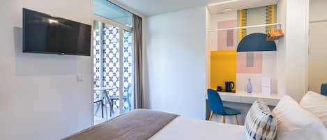 A modern hotel room with a bed, a desk, a chair, and a television.