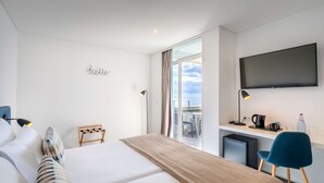 Habitación de hotel con cama, escritorio, silla, televisión y vistas al cielo.