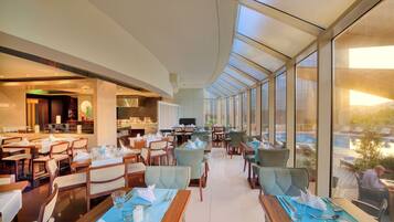 A modern restaurant with a high ceiling and large windows. Tables are set with white tablecloths and silverware.