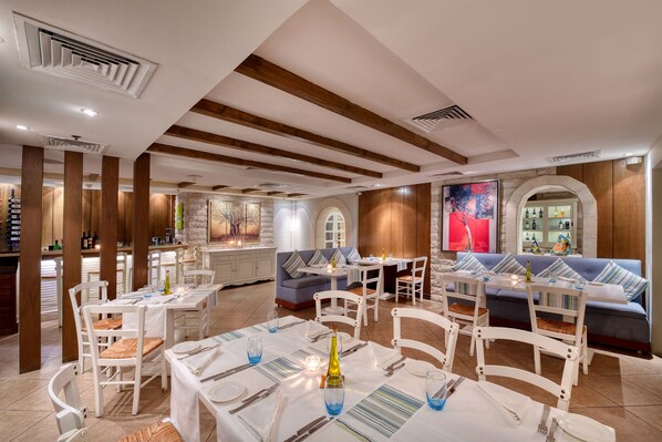Un restaurante con mesas y sillas blancas, una pared de piedra y un sofá azul.