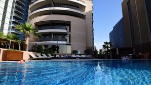 Una piscina con sillones de descanso y palmeras, rodeada de edificios modernos.