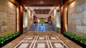 Un vestíbulo de hotel con piso de mármol, paneles de madera y una escalera que conduce a los pisos superiores.