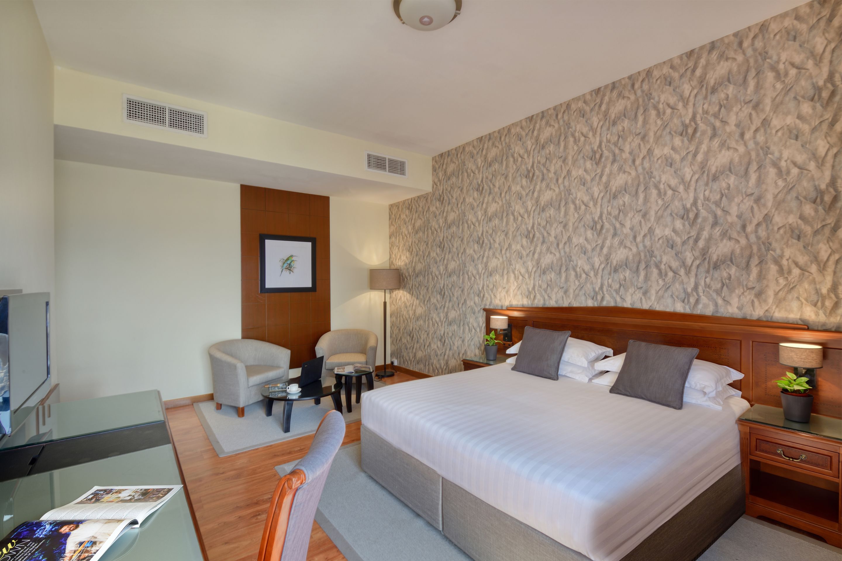 Habitación de hotel con una cama grande, un escritorio, una silla, un televisor y un cuadro colgado en la pared.