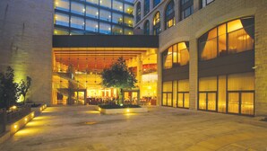 Un hotel con diseño arquitectónico moderno, que presenta un amplio patio con zonas de estar y un árbol central.
