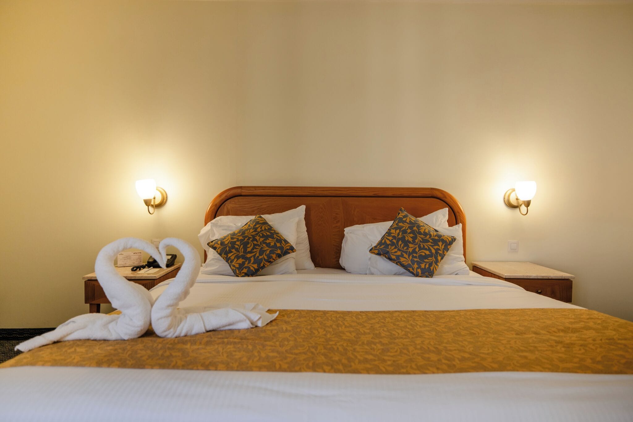 Habitación de hotel con una cama bien hecha, dos almohadas, una mesita de noche con una lámpara y una lámpara de pared.