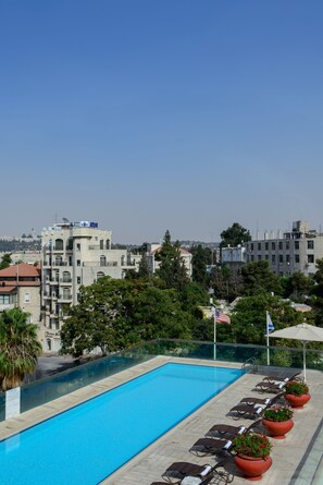 Una piscina en la azotea con sillones de descanso y plantas en macetas, rodeada de edificios y árboles.