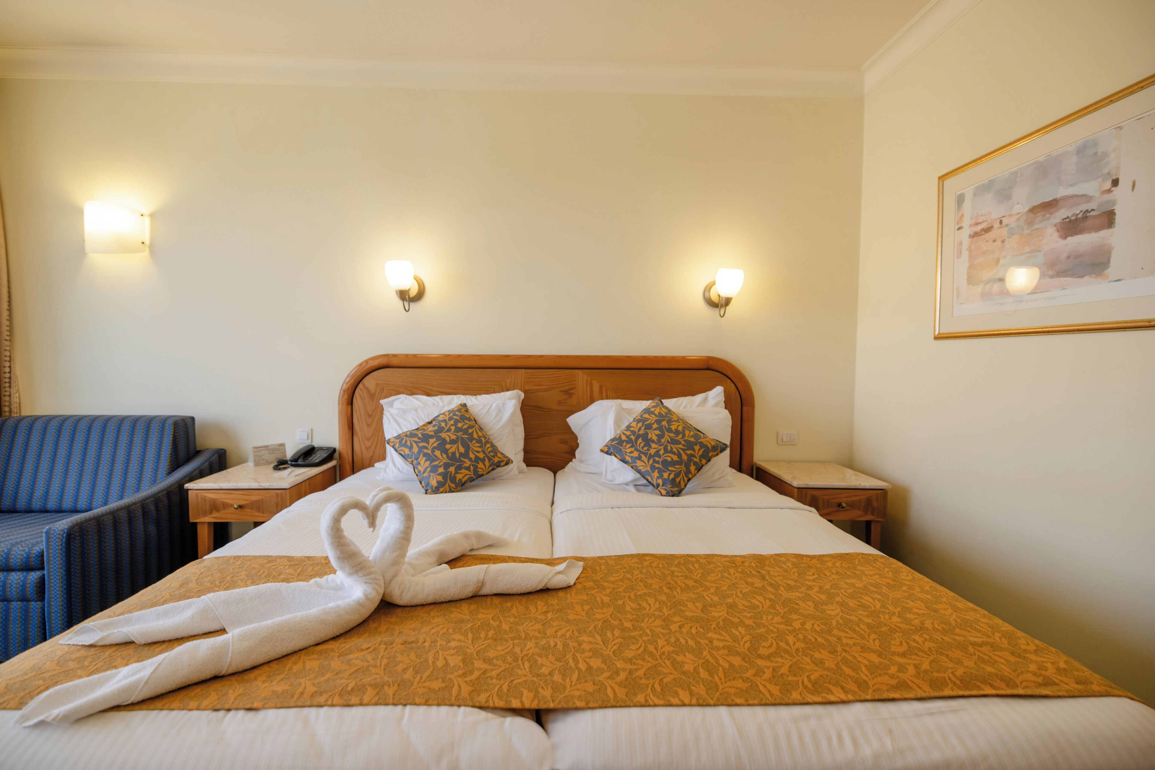 Ein Hotelzimmer mit einem Bett, zwei Nachttischen, einem blauen Sessel und einem Bild an der Wand.