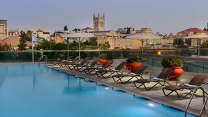 Piscina en la azotea con tumbonas y plantas en macetas, con vistas a un paisaje urbano histórico y una torre destacada.