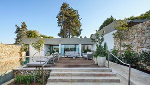 Un espace de vie extérieur moderne doté d’une piscine, de quelques marches menant à un coin salon et d’un mur en pierre.