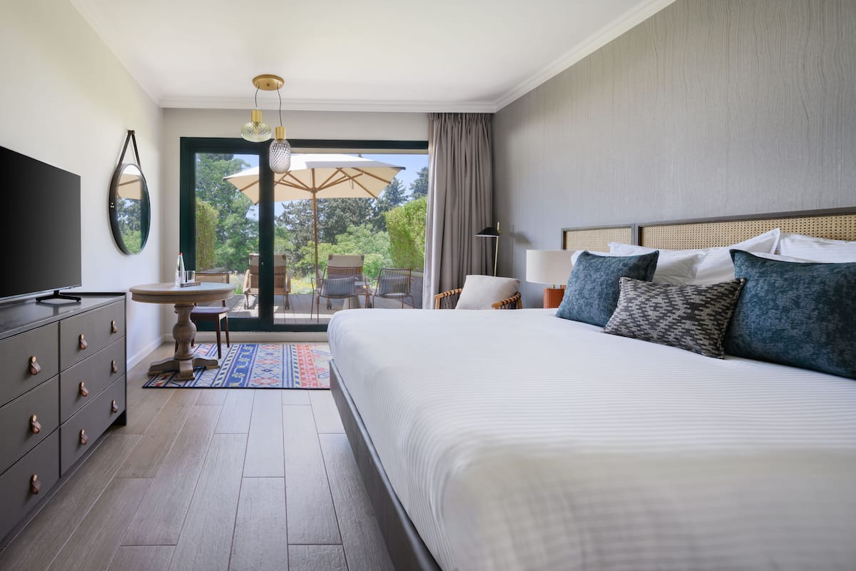 Ein modernes Hotelzimmer mit einem großen Bett, einem Fernseher, einem Esstisch und Blick ins Freie.
