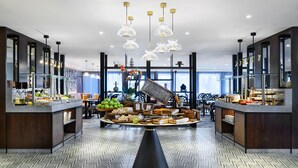 Un hall d’hôtel moderne avec une table ronde centrale où sont présentés des plats et des boissons, entourée de sièges et d’éléments décoratifs.