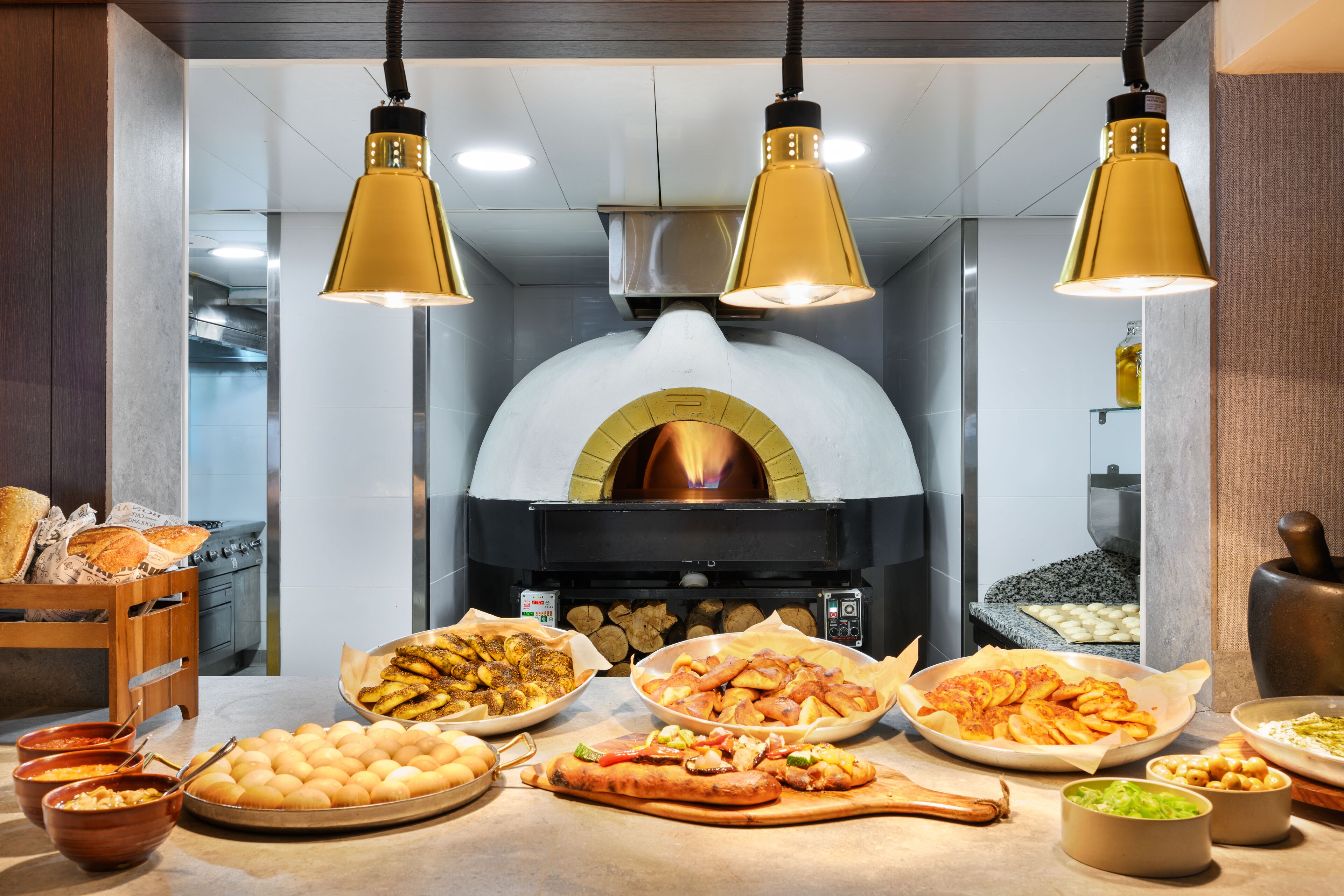 A kitchen with a wood-fired oven, various baked goods, and cooking utensils.