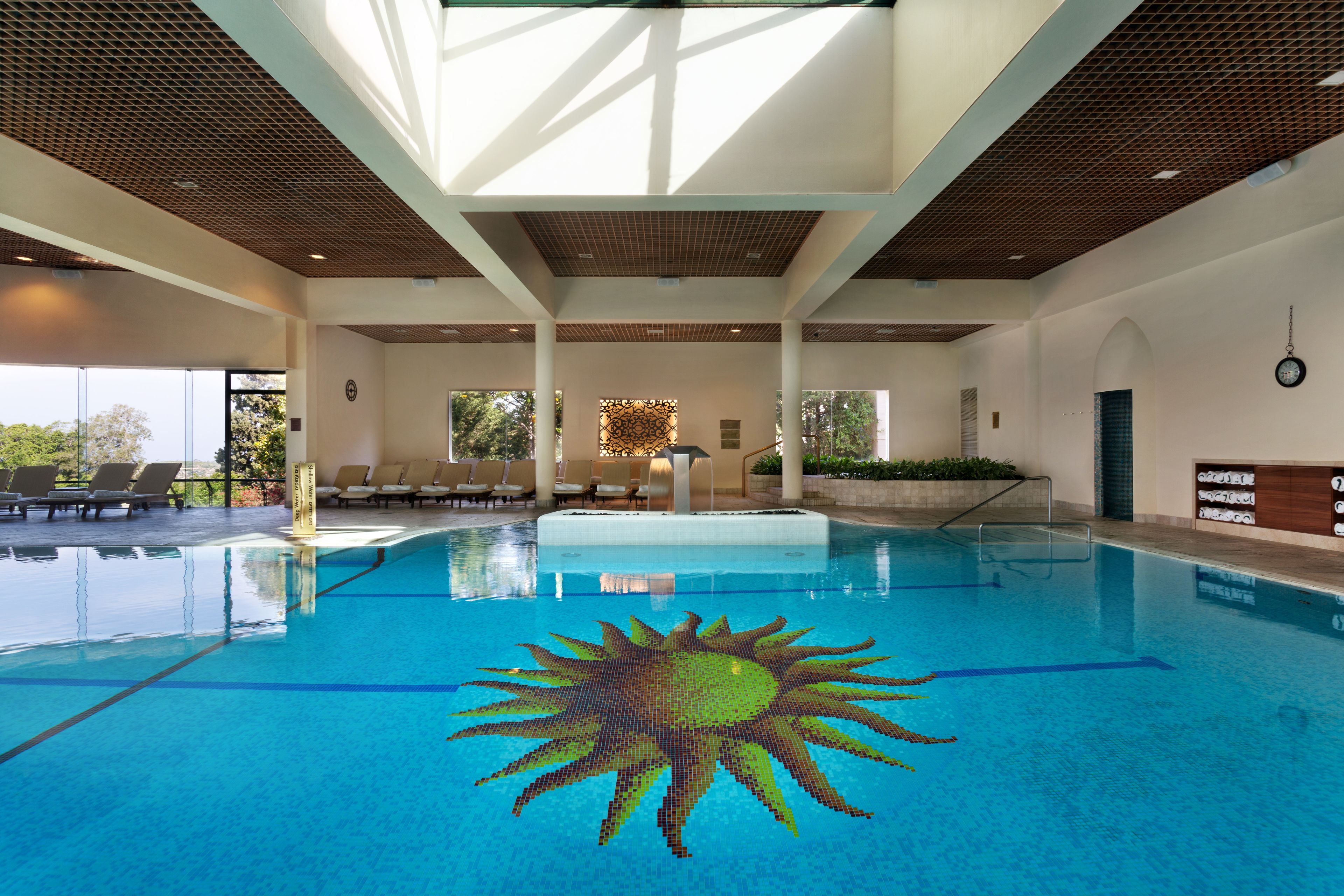 Una piscina con un diseño de mosaico solar, sillas de descanso y vistas al exterior.