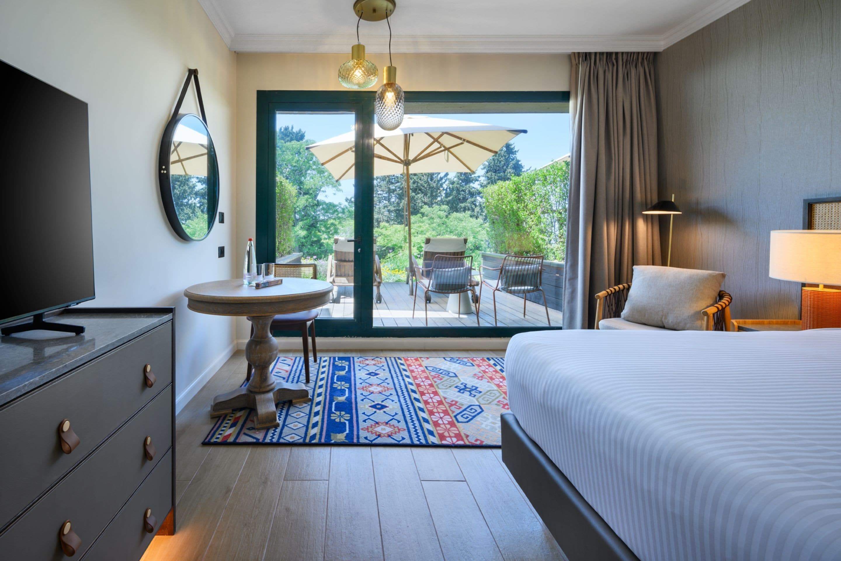 A hotel room with a bed, a television, a desk, and a view of the outdoors.