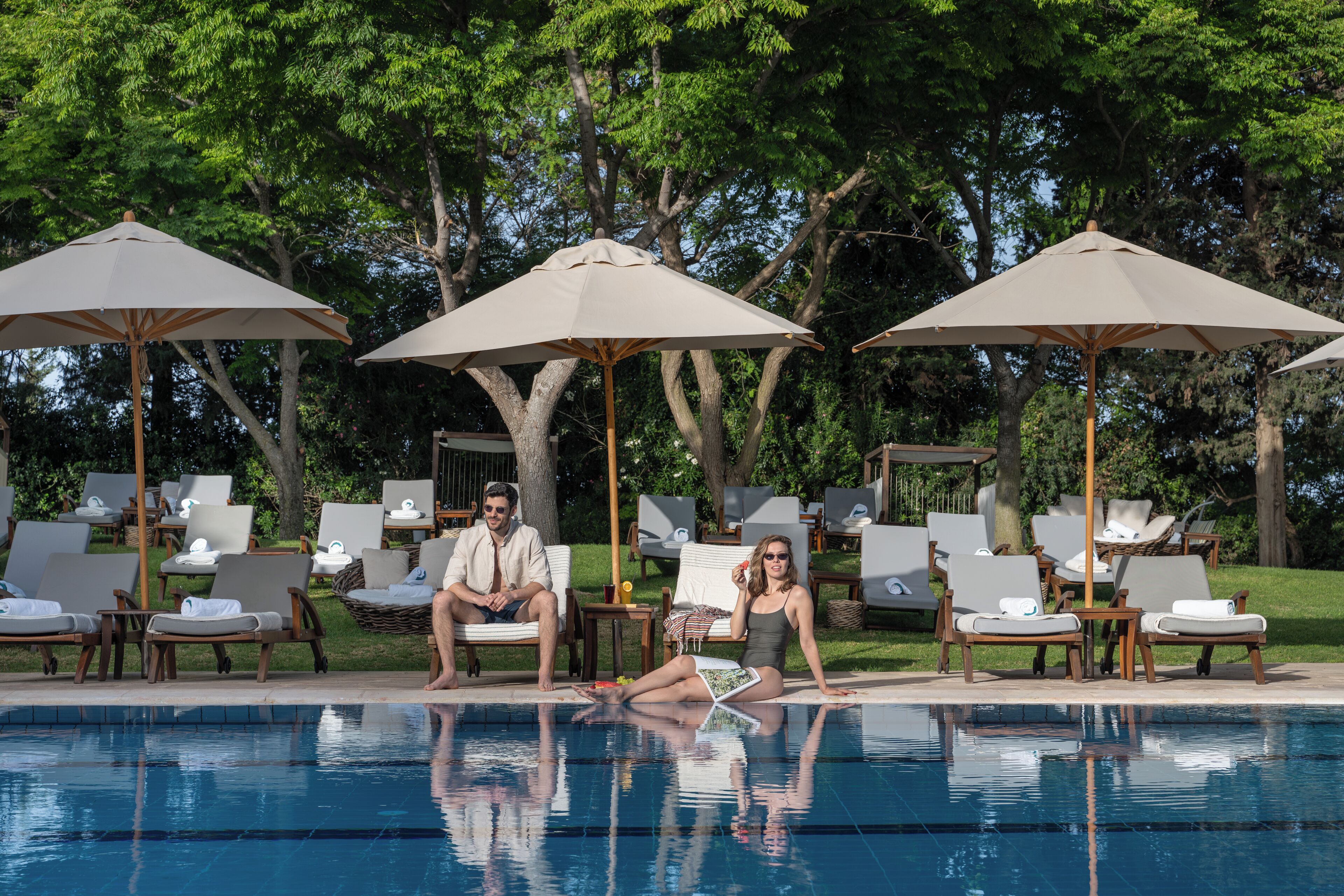 A poolside area with lounge chairs and umbrellas, surrounded by trees.