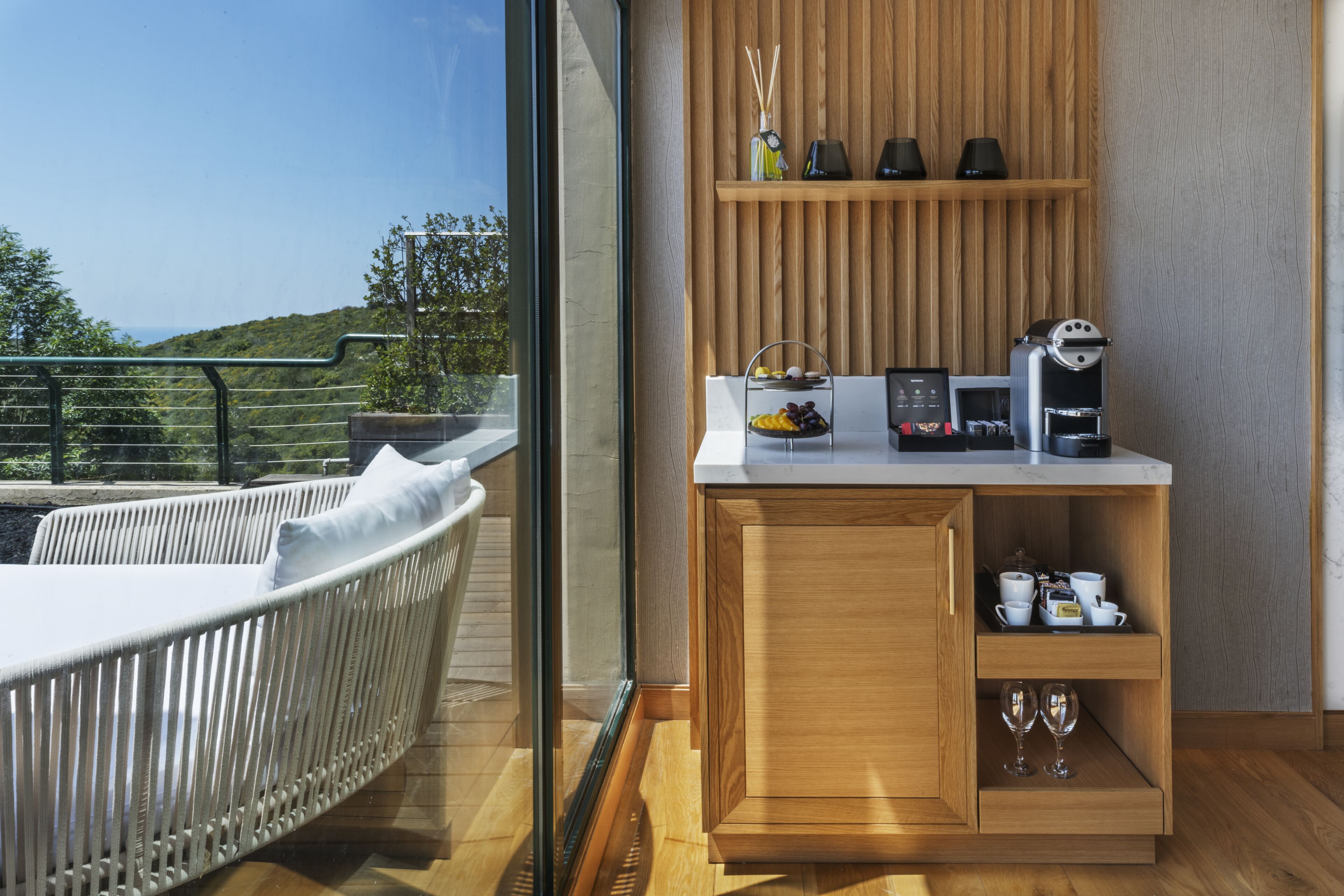 Een moderne kamer met balkon, een houten kast met koffiezetapparaat en een rieten bank.