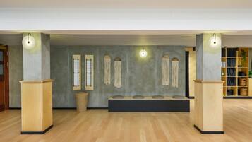 A spacious room with wooden flooring, a central seating area with cushions, and two wooden cabinets with light fixtures.