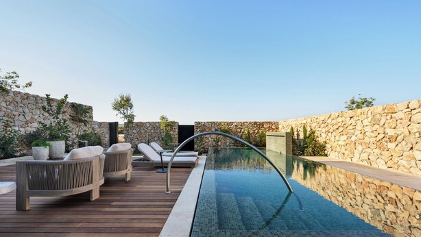 Une piscine extérieure avec des murs en pierre, une terrasse en bois et des chaises longues.