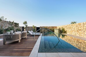 Piscina esterna con pareti in pietra, terrazza in legno e lettini.