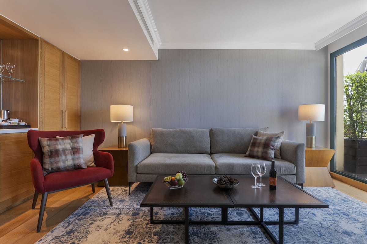 Ein modernes Wohnzimmer mit einem roten Sessel, einem grauen Sofa und einem Couchtisch mit Obstschale und Weingläsern.