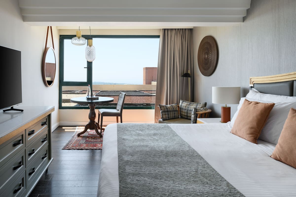 Ein Hotelzimmer mit einem großen Bett, einem Fernseher, einem Esstisch mit Stühlen, Blick ins Freie und einem Balkon.