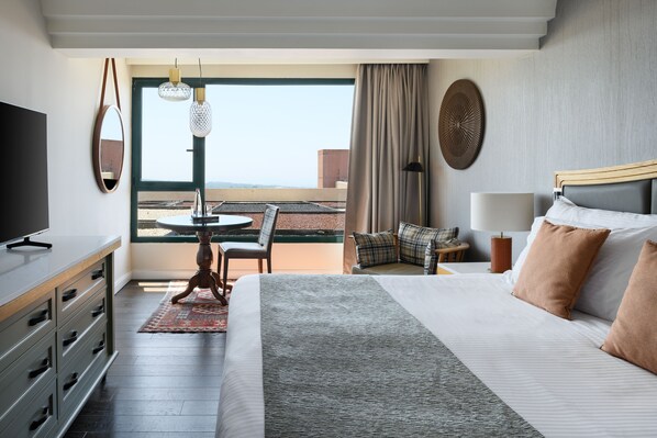 A hotel room with a large bed, a TV, a dining table with chairs, a view of the outdoors, and a balcony.