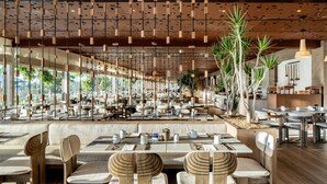 A spacious restaurant with high ceilings, hanging light fixtures, and a variety of seating arrangements including tables and booths.