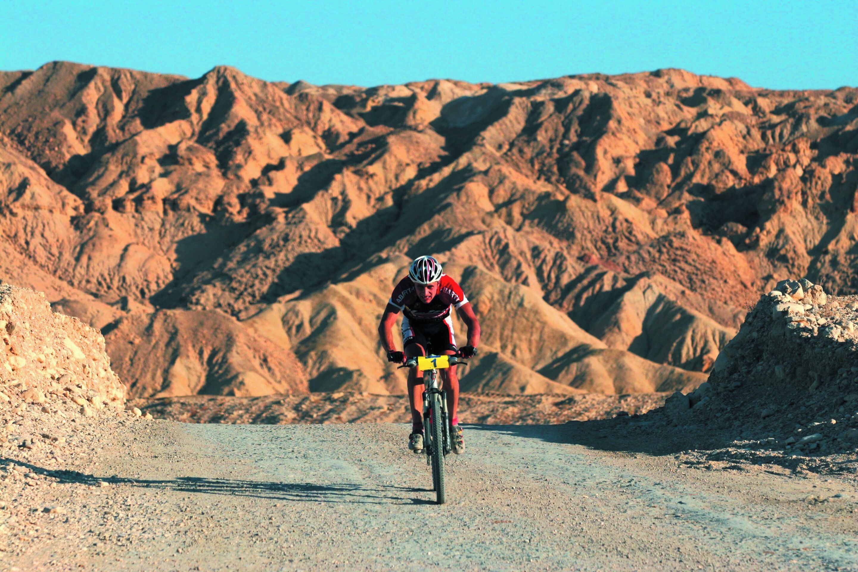 Un ciclista en un camino de tierra con montañas escarpadas al fondo.
