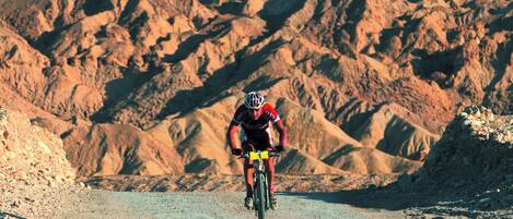 Un ciclista en un camino de tierra con montañas escarpadas al fondo.