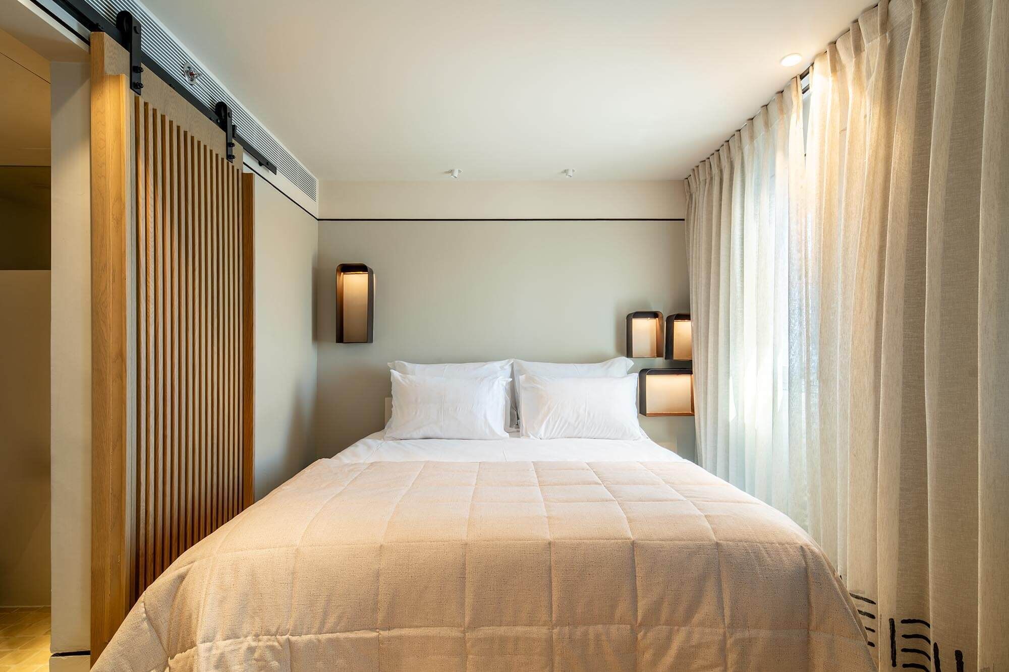 Een hotelkamer met een bed, twee wandlampen en een schuifdeur.
