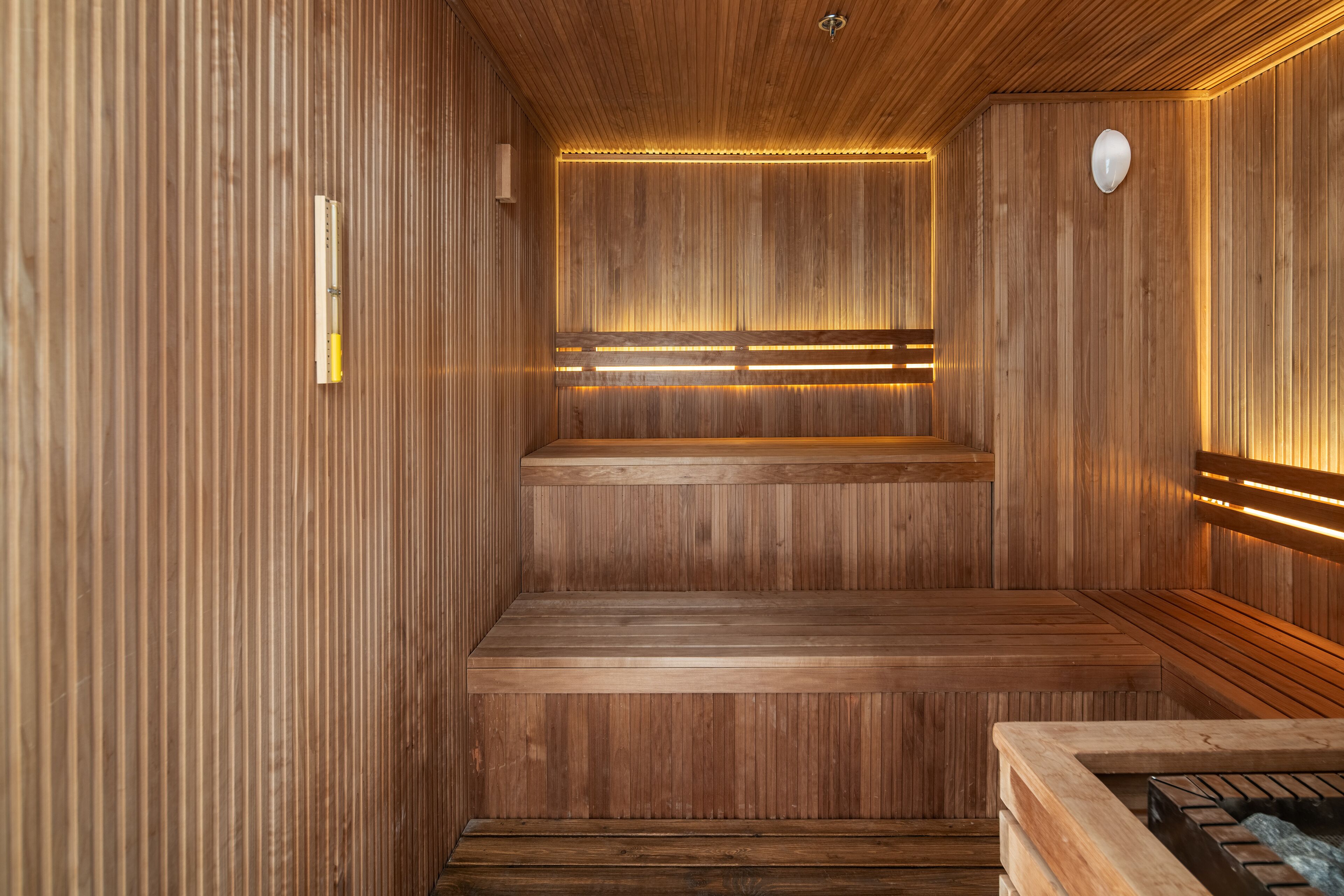 A sauna with wooden walls and benches, a bench in the center, and a small heater on the right.