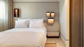 Une chambre d’hôtel moderne avec un grand lit, deux tables de chevet, une petite table et un luminaire fixé au mur.