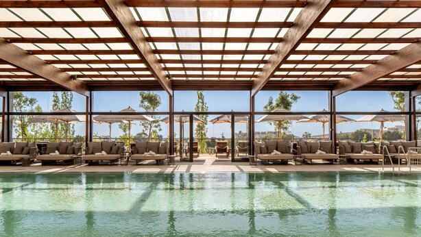 An indoor pool area with wooden beams, lounge chairs, and umbrellas.