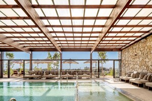 A pool area with lounge chairs and umbrellas, a stone wall, and a view of the outdoors.