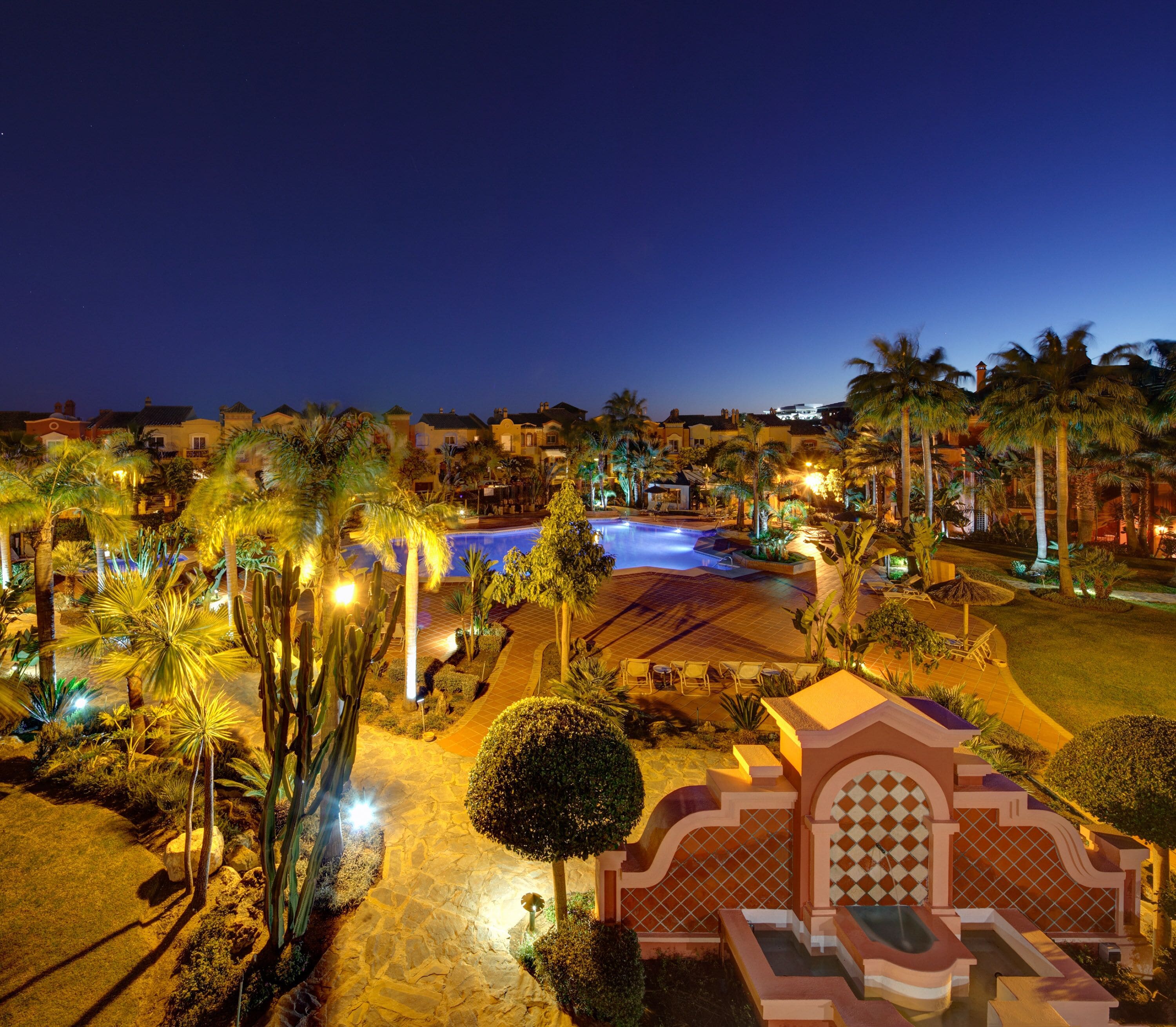 A resort with a swimming pool, palm trees, and a well-lit patio area.