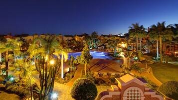 A resort with a swimming pool, palm trees, and a well-lit patio area.