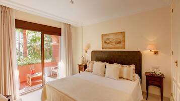 A hotel room with a large bed, a nightstand, a lamp, a painting on the wall, and a view of the outdoors through a sliding door.