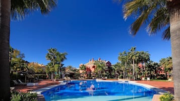 A swimming pool surrounded by palm trees and a red-roofed building.