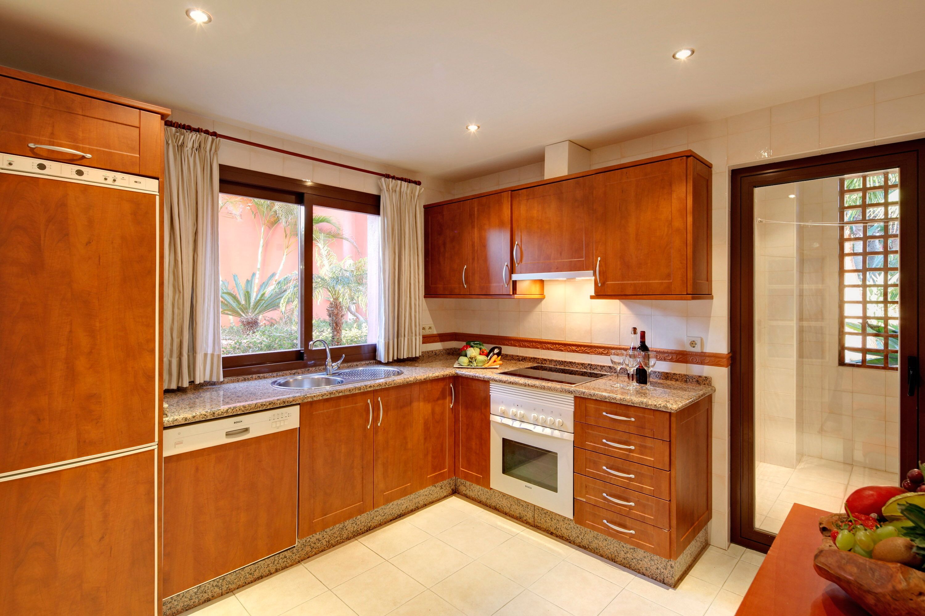 A kitchen with wooden cabinets, a built-in oven, and a window with curtains.