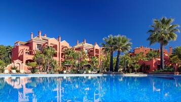 A hotel with a large pool, palm trees, and a clear blue sky.