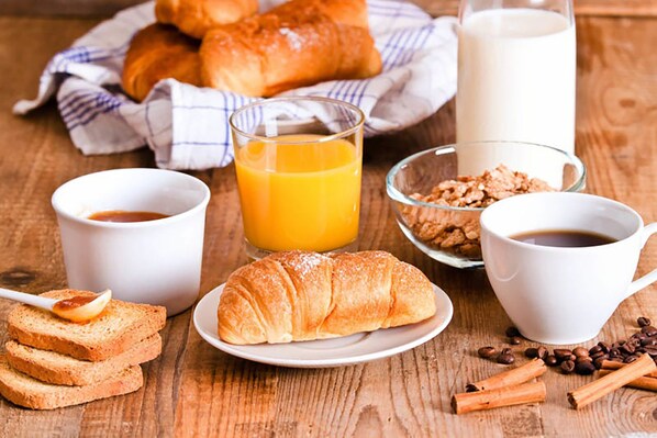 Een ontbijtsetting met croissants, sinaasappelsap, koffie en een kom granola.