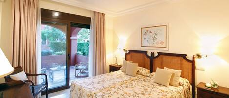A hotel room with a bed, a desk, a chair, a nightstand, and a view of the outside.