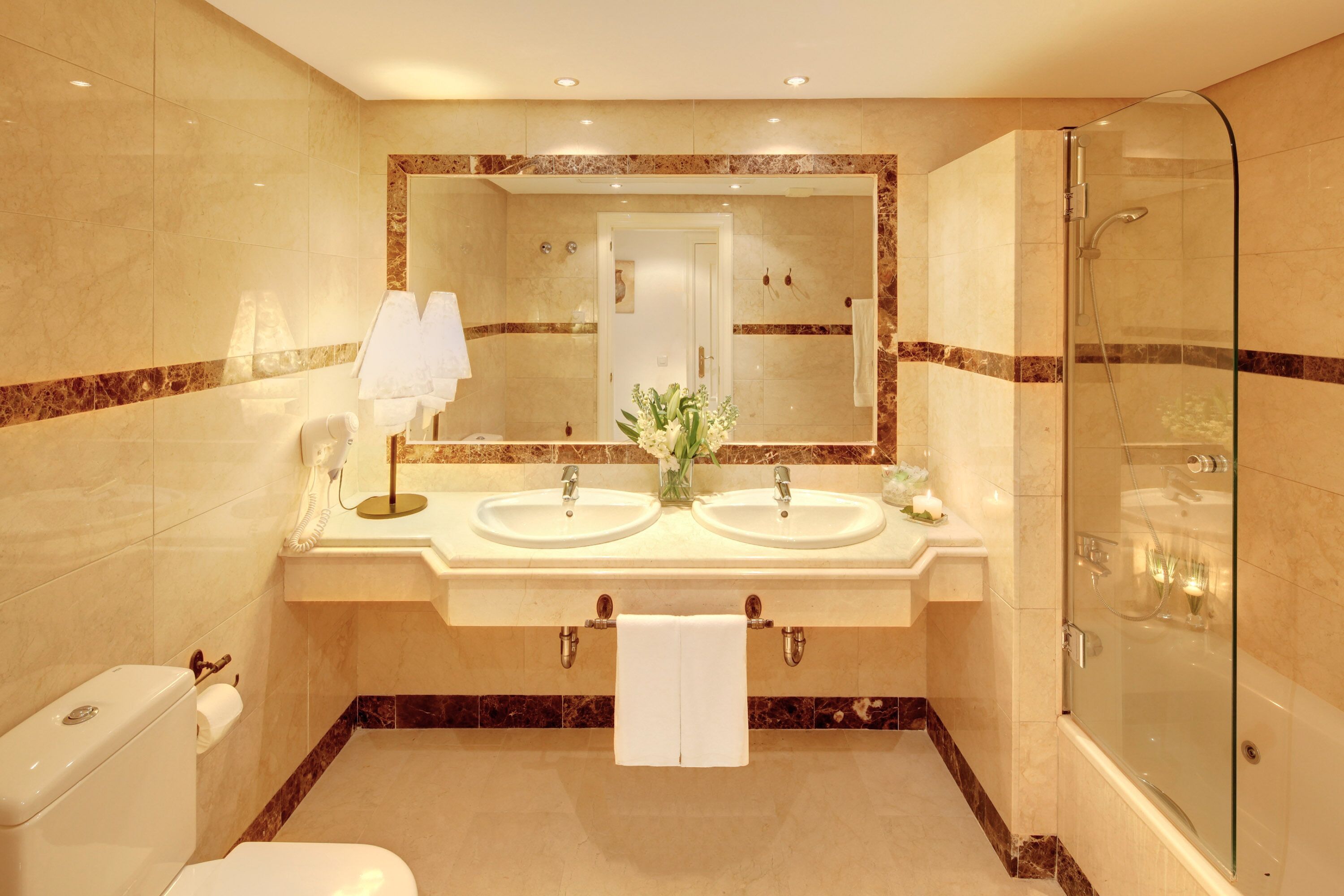 Une salle de bain moderne avec deux lavabos, un grand miroir, une douche en verre et des toilettes.