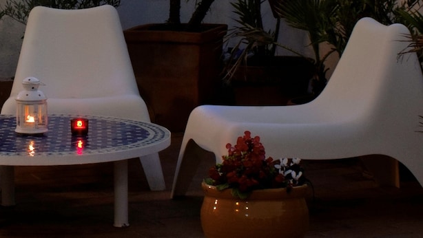 An outdoor seating area with white chairs and a round table, surrounded by potted plants and a view of a historic tower at dusk. - Hotel Un Patio en Santa Cruz (Seville)