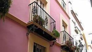 A pink building with a balcony, a window with bars, and a door. - Hotel Un Patio en Santa Cruz (Seville)